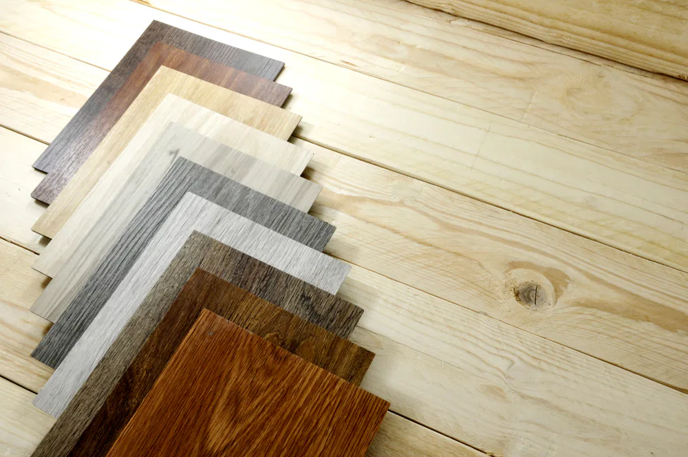 Various wood flooring samples displayed on a wooden floor, labeled as Crown Finish, showcasing different textures and colors.