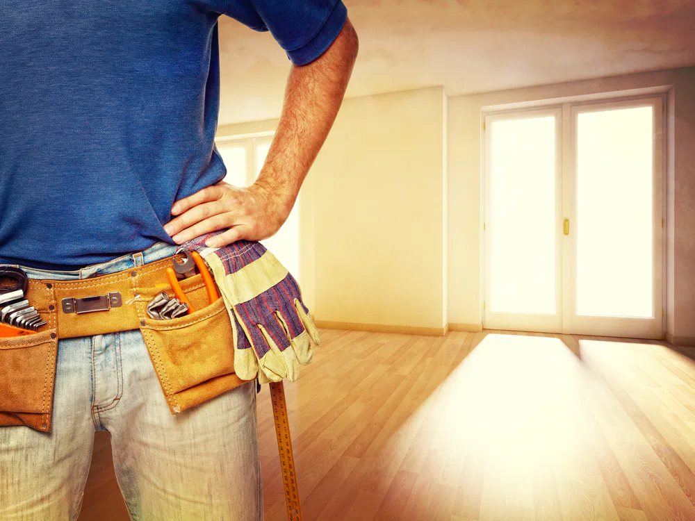 A man in a blue shirt and jeans holds a tool belt, representing Crown Finish's commitment to quality craftsmanship.