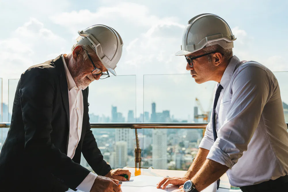 Two men in hard hats examining blueprints at a construction site, labeled 'Crown Finish'.