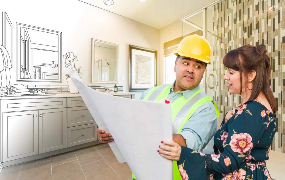 A man and woman examine a blueprint in a bathroom, discussing design elements for a project labeled 'Crown Finish.'