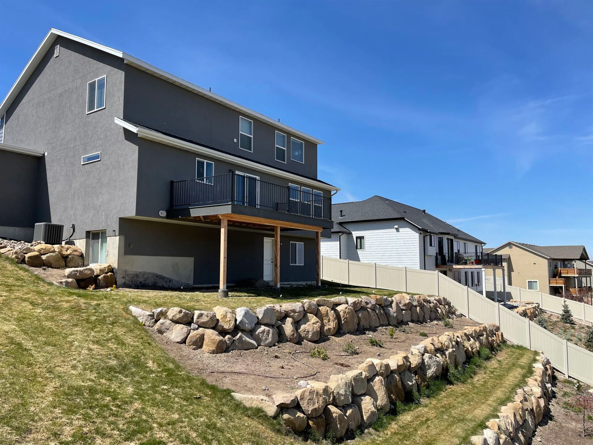 A house with a stone wall and a fence, featuring a design by Crown Finish, set against a clear blue sky.