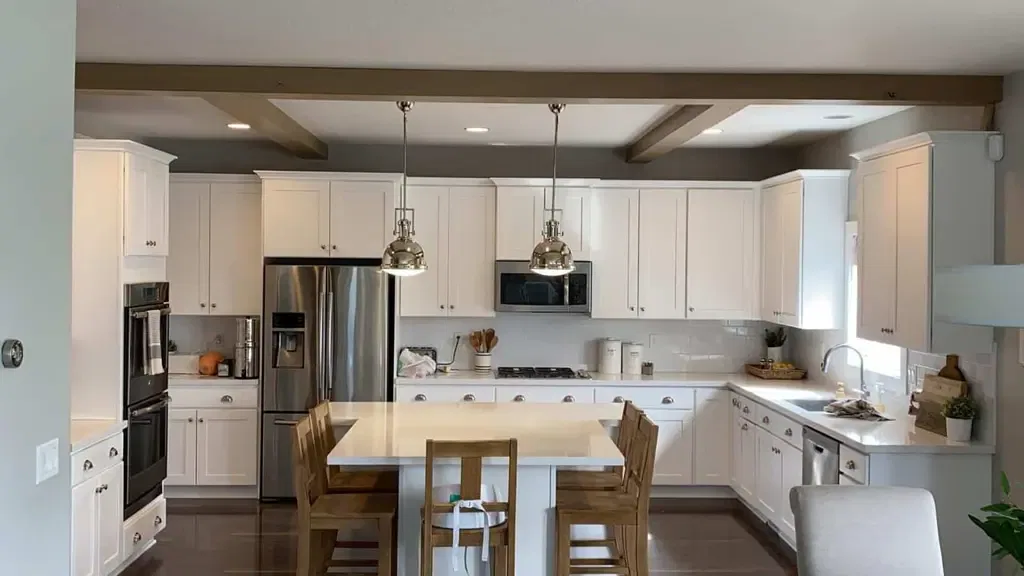 A modern kitchen with white cabinets, stainless steel appliances, a central island with wooden chairs, and pendant lighting.
