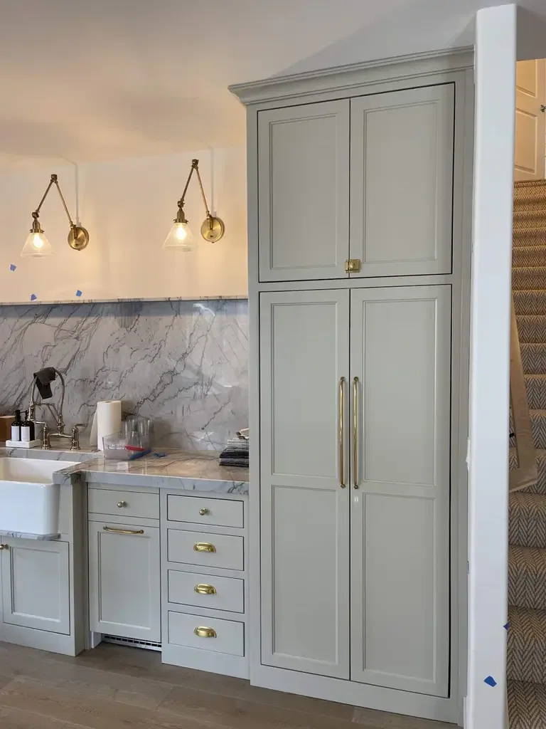 Modern kitchen with marble backsplash, brass hardware, and tall pantry cabinets.